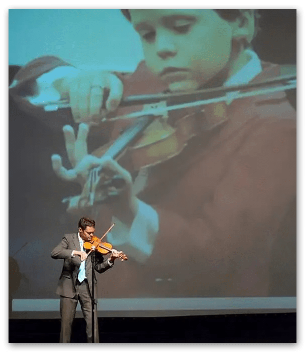 A man playing the violin in front of a large screen.